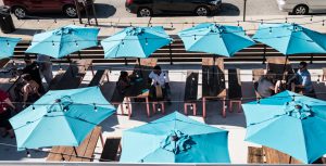 A bird's eye view of Pecan Penny's patio shows 7 teal tents on picnic tables, filled with patrons enjoying the great barbecue