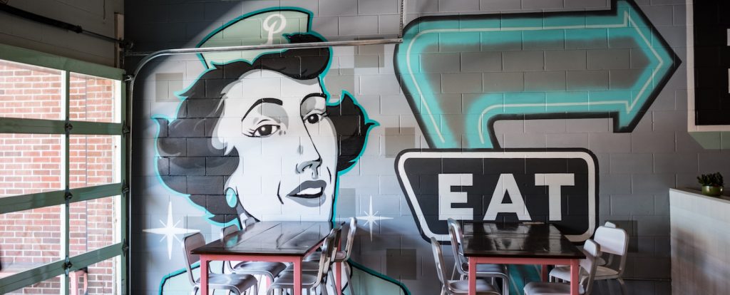 A mural of a woman in mid-century garb with a "P" hat and teal earrings adorns the East wall of Pecan Penny's restaurant